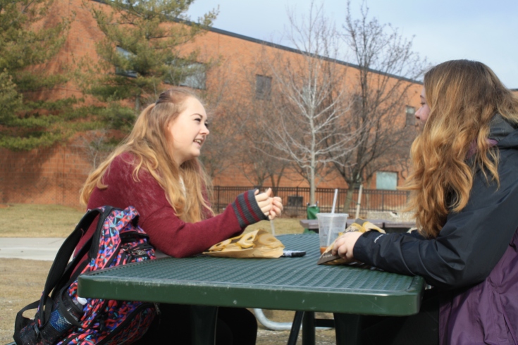 Freshmen Rhiannon Parise, left, and Rebekka Lange, right, soak up the warm weather in between classes outside of the EHS building on Thursday, Feb. 23.
